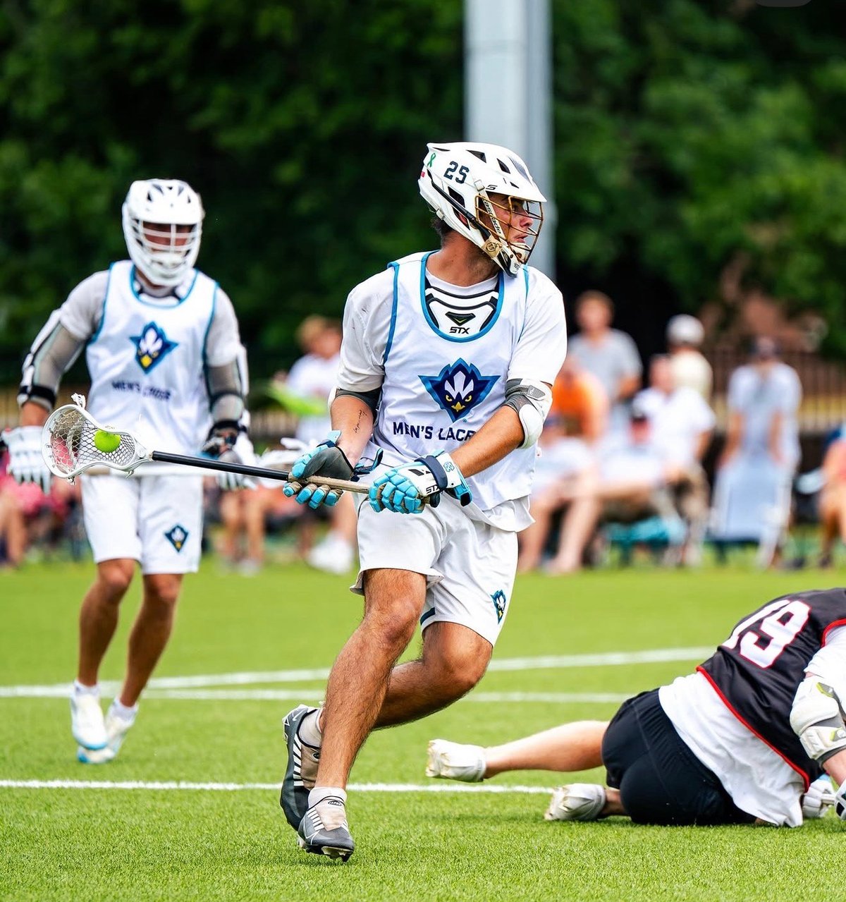 Lacrosse player in white uniform running with the ball while an opponent slides